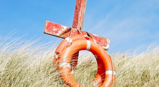 A cross and life preserver on a beachside hill.
