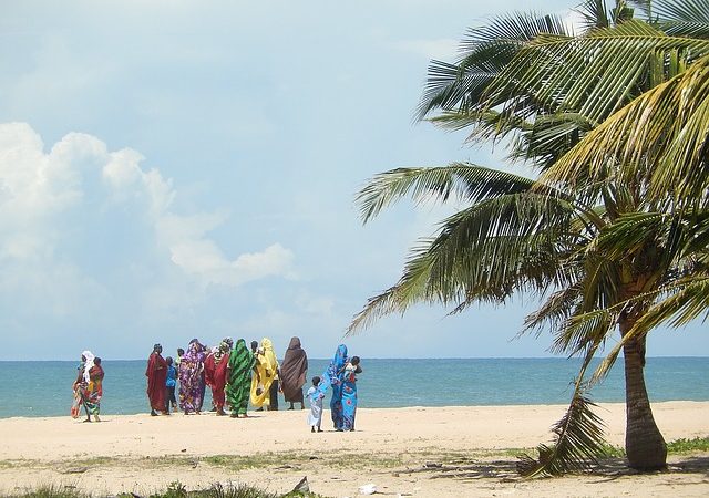 Women covered in veils on the beach from a distance.
