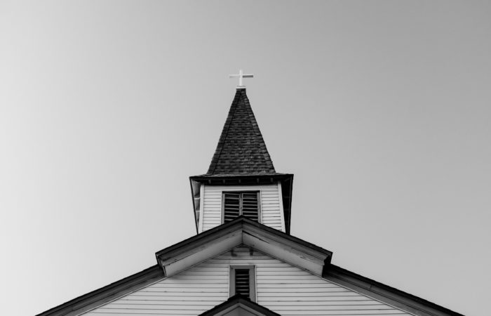 Black and white image of a cross on top of the steeple of a church