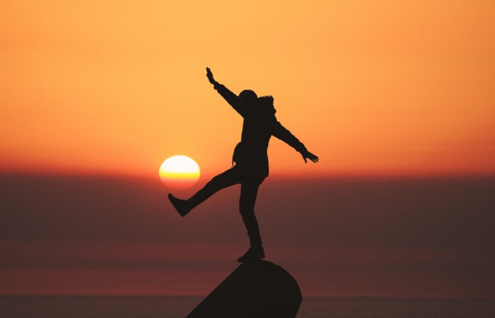 A person dancing on top of a rock at sunset