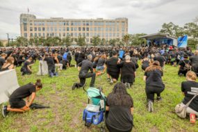 A number of people kneeling to pray in a large open field in front of a stage