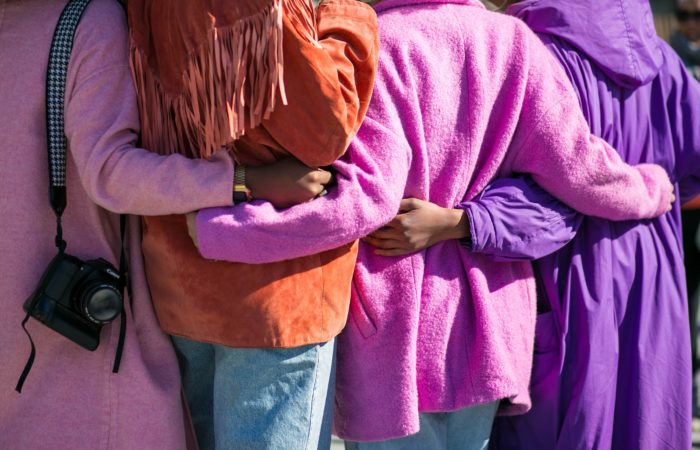A group of women in pink coats, seen from the back, with arms around each others' waists