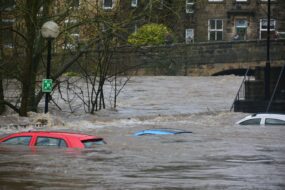 A flood on a city street which has covered cars so that only their roofs are showing