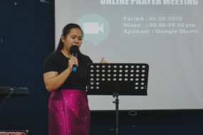 A woman with a music stand and microphone hosting a Sunday morning prayer service