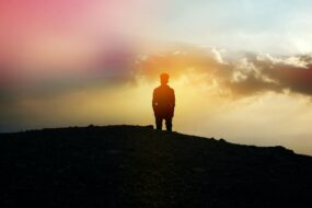silhouette of person standing on a hill looking at sunset
