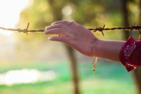 A woman reaching out her hand to touch a barbed wire fence