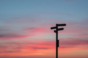 A signpost pointing different directions with a sunset behind it