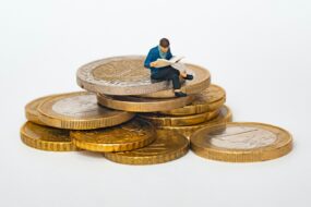 A miniature figure of a man sitting on a pile of coins